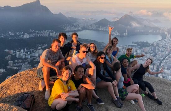 Hikers enjoying a scenic view from the summit of Dois Irmãos mountain, with Rio de Janeiro's skyline and coastline stretching out beneath them, bathed in golden sunlight.